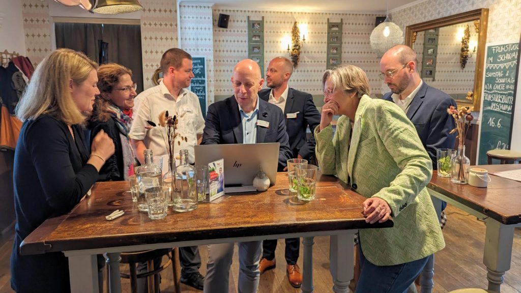 Mehrere Personen beim Brunch und Fachgesprächen schauen auf Laptop