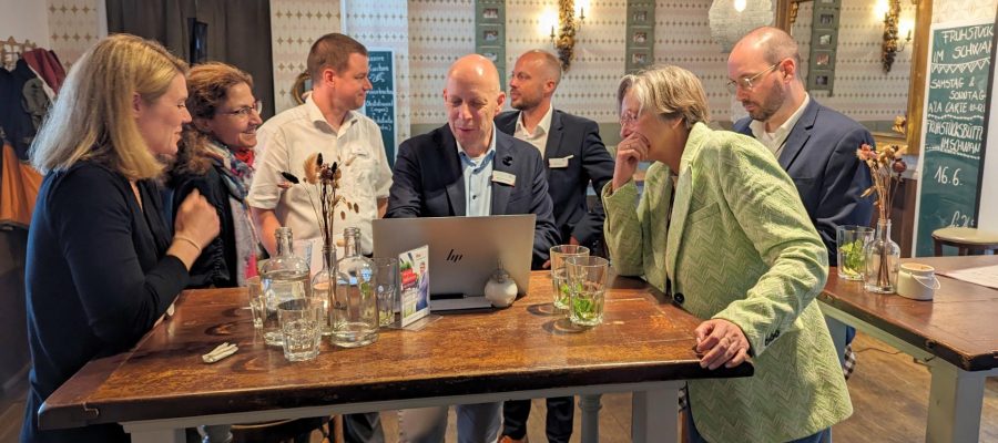 Mehrere Personen beim Brunch und Fachgesprächen schauen auf Laptop